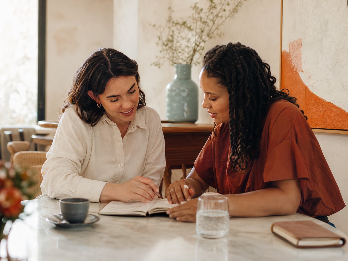 Two people talking over a notebook at a bright table